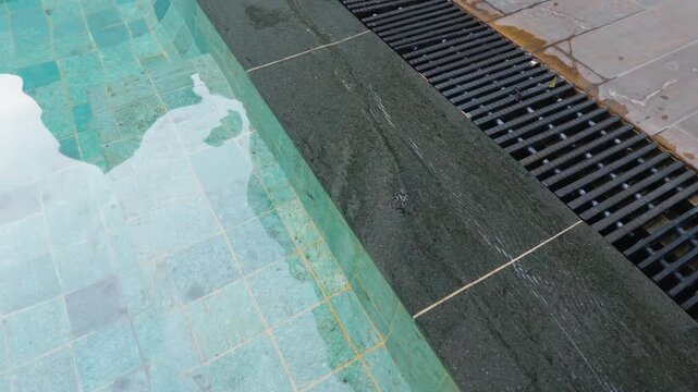 Modern swimming pool edge with turquoise water stone coping and overflow drainage grate.