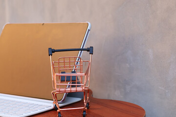 Miniature shopping cart in front of an open tablet with blank mockup screen on wooden table, online shopping and digital commerce concept. © Isman