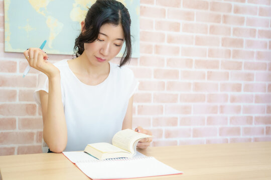 Japanese woman raising a pen in a moment of realization while studying at a desk