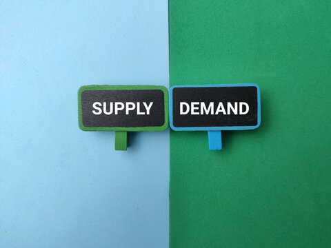 Two mini signboards marked SUPPLY and DEMAND sit side-by-side against a split blue and green paper background