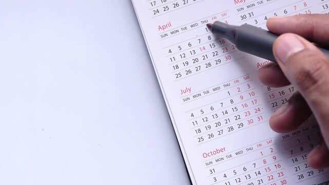 Person marking specific dates on calendar with red marker for planning and scheduling