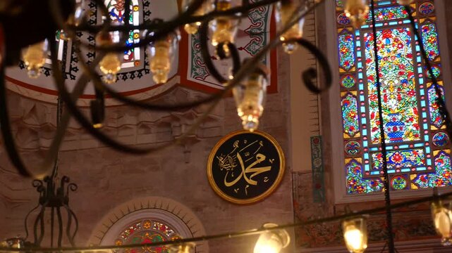 Ornate stained glass window illuminates mosque interior with calligraphy and chandelier motion
