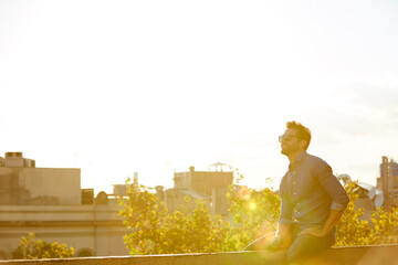 Obraz premium Man, travel or thinking on terrace with space in city for sunset view, vacation or holiday. Happy, male person or tourist relaxing with sunglasses or smile on outdoor balcony for weekend trip in town