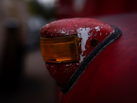 Close-up detail of a weathered amber signal light on an old red Scania fire truck, showing chipped paint, rust and signs of age.