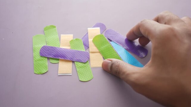 Close up of person hand picking up colorful medical bandages from table