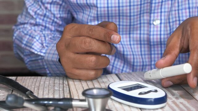 Close up shot of man checking his sugar level for diabetes while sitting at table for regular health check up with medical equipment such as stethoscope