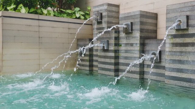 Modern decorative water fountain spouts pouring into a luxury swimming pool.