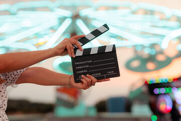 Hands Holding Movie Clapperboard At Colorful Amusement Park Neon Fairground. Person holding a black cinema clapper board against bright  carnival lights © nicoletaionescu