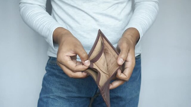Man showing empty wallet and palms with no money or credit cards inside brown leather pocket against white background