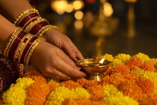 Woman lighting traditional oil lamp with marigold flowers