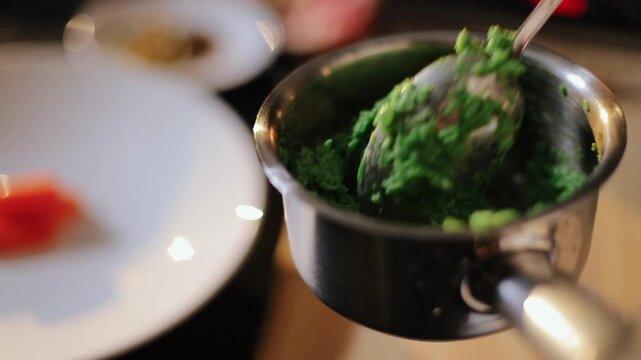 Metal spoon lifts textured bright green mash from small stainless steel container, spoon angled from top-right with portion held above bulk mixture showing clear scooping and portioning state