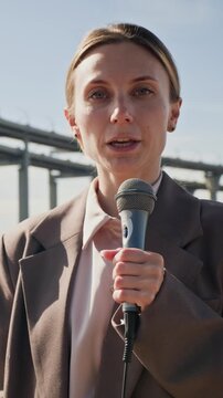 Portrait of Caucasian young adult woman journalist reporting live with microphone about ecological disaster. Video suitable for environmental news broadcasts, vertical