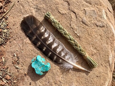 Natural smudge bundle with eagle feather and raw turquoise stone resting on desert sandstone for traditional spiritual smudging rituals and ceremonies.