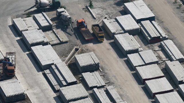 Trucks moving across a large industrial site filled with stacked concrete piles and materials
