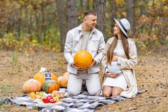 A pregnant woman and her partner celebrate their upcoming baby with pumpkins and a picnic in the autumn forest