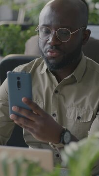 African American man office worker making online video call using smartphone talking to colleague at work. Virtual meeting and communication concept.