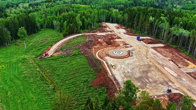 Aerial view of ongoing construction site in a lush green forest clearing during daytime with cloudy sky drone footage.