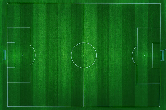 Aerial top-down view of a professional football field with vibrant green grass and clear white markings. The pitch is empty, perfectly manicured, and ready for a soccer match in a stadium at night.