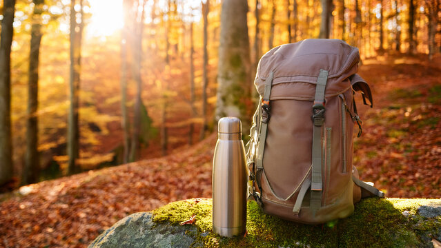 Canvas hiking backpack on mossy rock with blurred golden autumn forest background banner.
