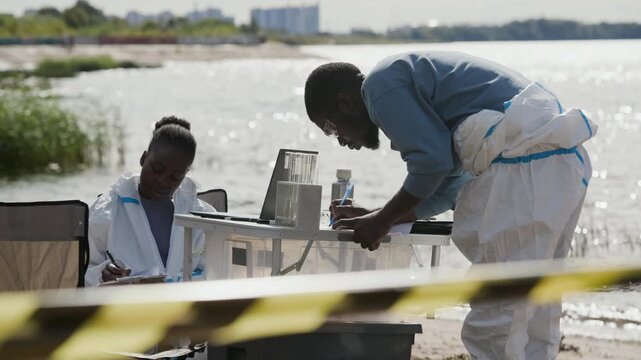 African American young adult man and woman writing research data near water testing station outdoors. Perfect for ecological disaster reports, pollution studies, and conservation videos