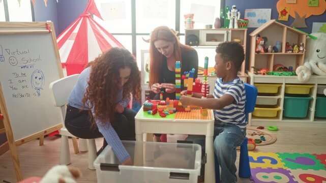 Woman teacher and boy build a tower of colorful blocks, woman reaches hand into plastic storage bin and points to pieces in classroom building; playful learning cooperation.