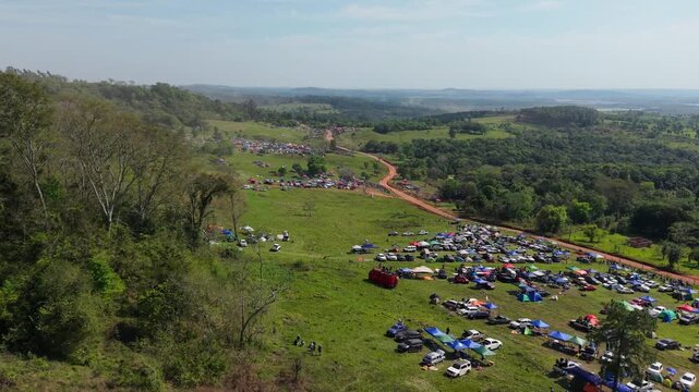Camping Rally 2026 fills a grassy campsite beside a winding rural road in Nueva Alborada, Itapua, Paraguay, South America, with tents, cars and campers spread across the countryside, drone forward fly