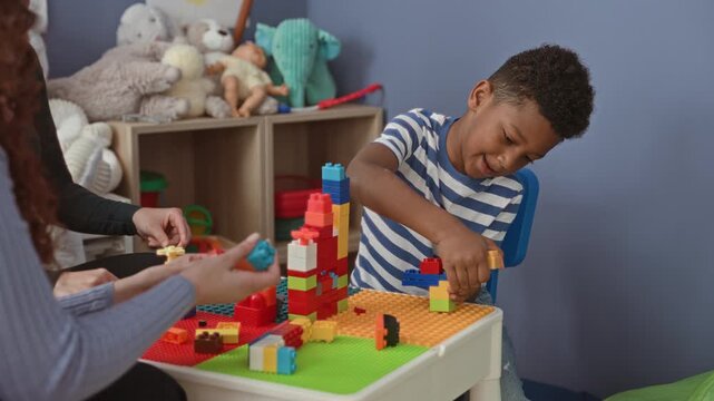 Boy building a colorful block tower with hands at a preschool activity table inside a building; focused learning.