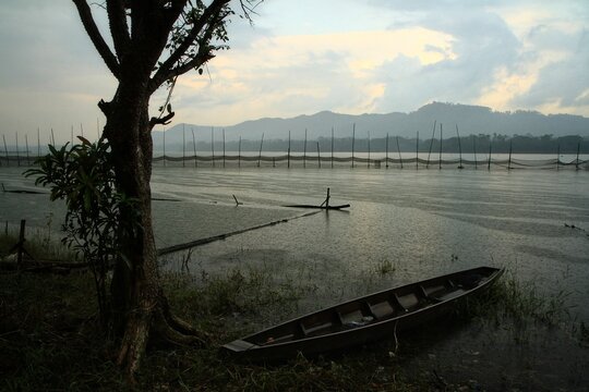 Traditional wooden boat on lake shore during rainy day with mountains background