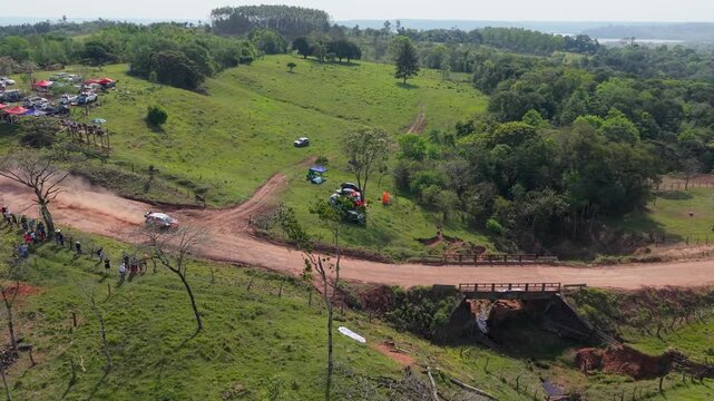 Dynamic drone shot captures a lively crowd along a rural dirt road as rally cars speed by, raising dust during the WRC Rally 2026 under clear daylight in lush Paraguayan countryside.