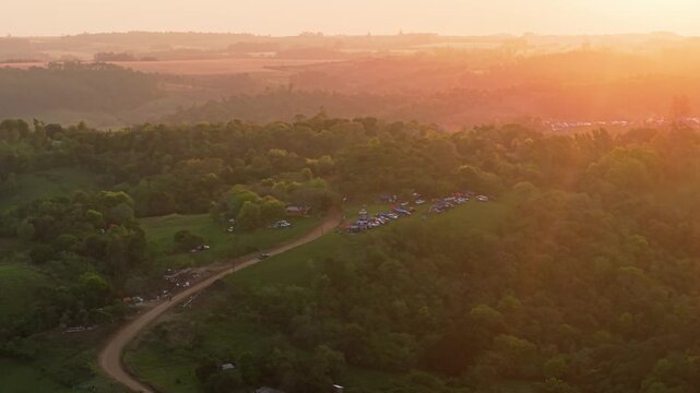 Drone video captures the golden glow over lush hills with clustered tents and cars at the WRC Rally 2026 camping area in Nueva Alborada, Paraguay during a scenic sunset.