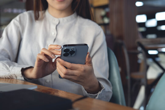 Asian business woman using smartphone with laptop computer and notebook on table, online working at modern office, closeup. Woman using mobile phone for social media network.