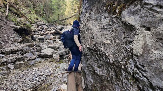 Hiker traversing narrow wooden plank path along rocky mountain cliffside in scenic gorge.