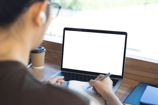 Mockup blank screen laptop, woman working laptop and writing in notebook at cafe for web template or application design, social media marketing