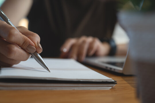 Close up, woman writing in notebook while working on laptop, online business and modern remote work concept.