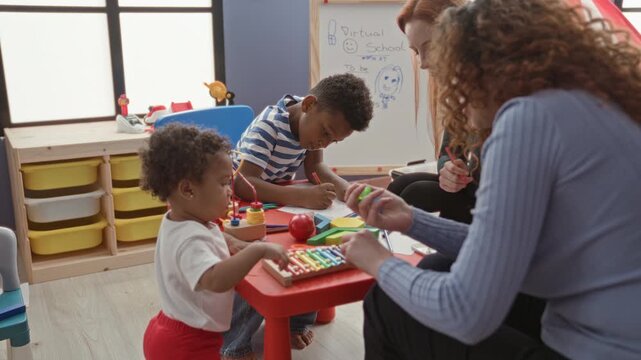 Woman helps boy draw with colored pencil at a red play table strewn with xylophone and toys in a classroom; playful learning care.
