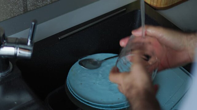 person washing dishes in a modern kitchen sink. Domestic chores, household duties, daily routine, and clean tableware concept with running water and blue plates.