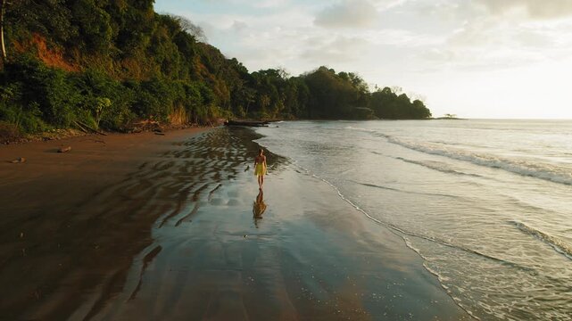 Woman walks on wet sand during golden hour at Dominicalito Beach Costa Rica