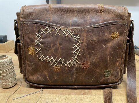 repaired leather bag without branding Vintage brown leather bag with hand-stitched patch repair on wooden table.
