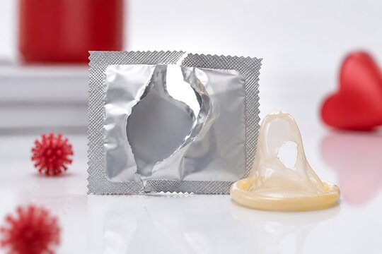 Single condom package with open wrapper and latex barrier against red heart backdrop during studio lighting