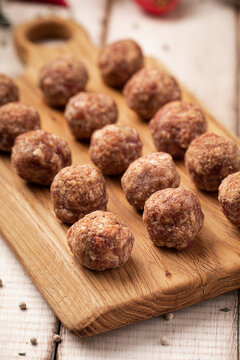 Uncooked minced beef meat balls for cooking on rustic wood board with herbs and tomatoes on white table