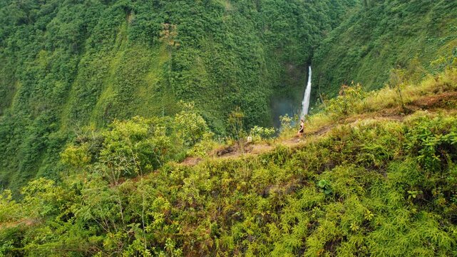 Traveler woman hiking along mountain trail overlooking rainforest waterfall