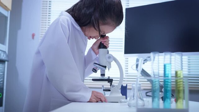 Asian girl student looking through microscope in science laboratory for stem education and biotechnology learning	