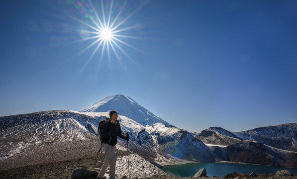 Hiking Tama Lake Tracks in winter. Sun starbursts shining over Upper Tama Lake and snow-capped Mount Ngauruhoe. Tongariro National Park. New Zealand.