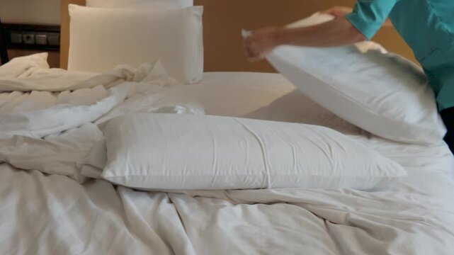 Hotel housekeeper changing sheets and arranging pillows on a large comfortable bed in a luxury room.