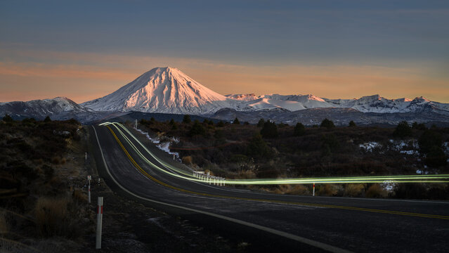 Long exposure image of car light trail on Desert Road at dawn. Snow-capped Mt Ngauruhoe in the distance. North Island. New Zealand.