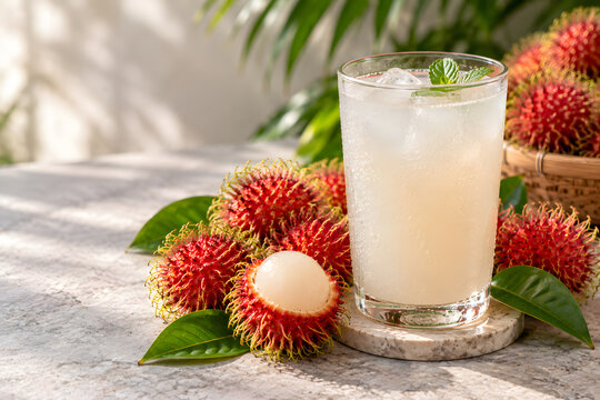 Cold refreshing rambutan juice glass with ice and mint next to fresh rambutan fruits on stone table.