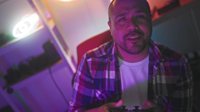 Man smiles and fist pumps while seated in gaming chair in studio, gesturing to camera during game streaming; victory joy.