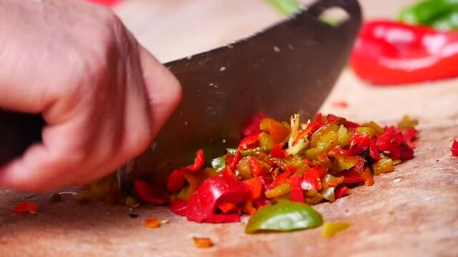 Chopping red and green peppers on a wooden cutting board with a large knife