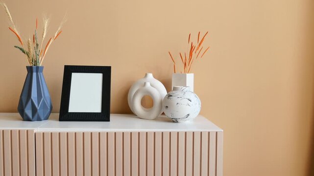 Minimalist interior design featuring modern vases and frame on white wooden sideboard against beige wall