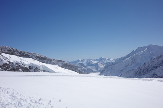 A broad glacier basin rimmed by rocky snow-covered ridges opens toward distant peaks under a clear blue sky near Lauterbrunnen, Switzerland